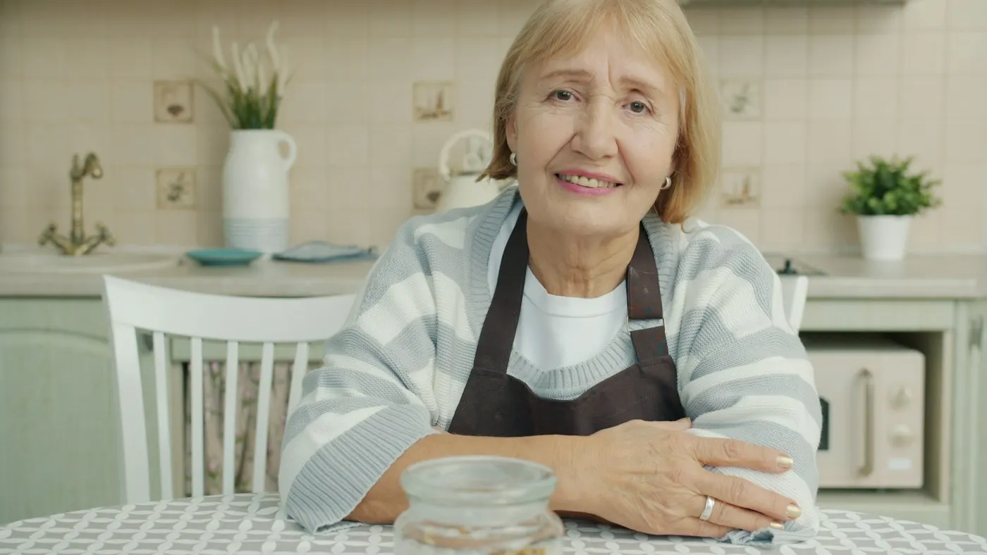 Signora anziana sorridente seduta al tavolo della cucina